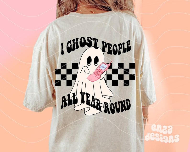 May include: Cream-colored t-shirt with a graphic of a ghost holding a pink flip phone. The text "I Ghost People All Year Round" is above and below the ghost, with a black and white checkered pattern.