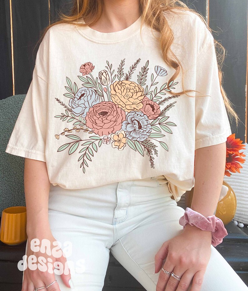 May include: A cream colored t-shirt with a floral design featuring pink, blue, and yellow flowers with green leaves.