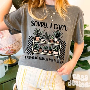 Puede incluir: Camiseta gris con un gr&aacute;fico de una estanter&iacute;a de plantas con el texto "Lo siento, no puedo, tengo que regar mis plantas".