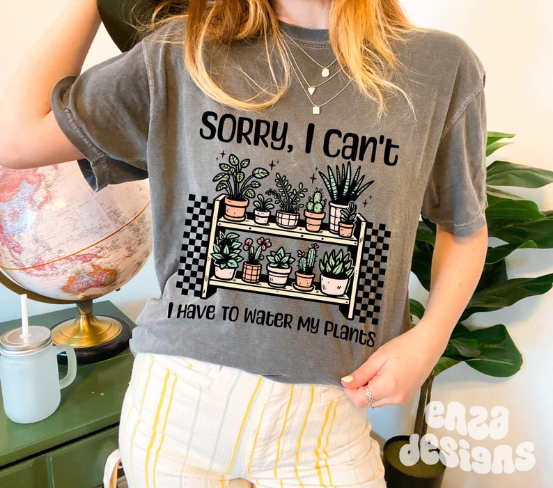 Puede incluir: Camiseta gris con un gr&aacute;fico de una estanter&iacute;a de plantas con el texto "Lo siento, no puedo, tengo que regar mis plantas".