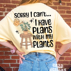 May include: A yellow t-shirt with the text "Sorry I can't... I have plans with my plants" and a cartoon image of a potted plant on a stool being watered by a watering can.