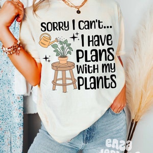 May include: A white t-shirt with the text "Sorry I can't... I have plans with my plants" and a graphic of a potted plant with a watering can.
