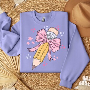 May include: A lavender sweatshirt with a graphic of a yellow pencil tied with a pink bow and surrounded by pink stars.