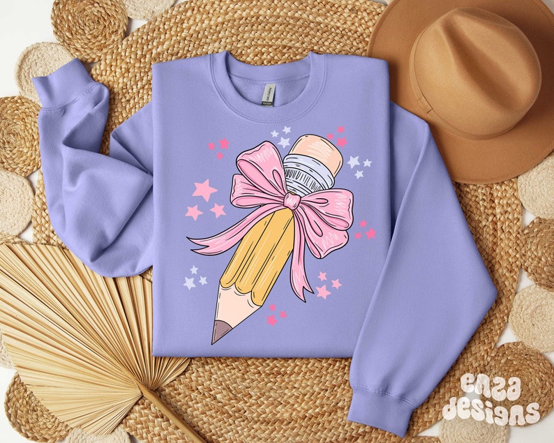 May include: A lavender sweatshirt with a graphic of a yellow pencil tied with a pink bow and surrounded by pink stars.