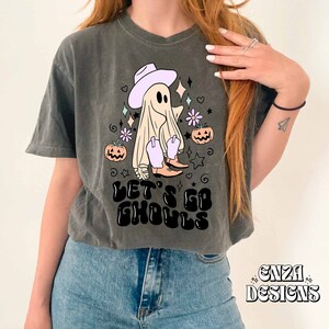 May include: Dark gray t-shirt with a Halloween-themed graphic. The design features a ghost wearing a cowboy hat and boots, with the text "LET'S GO GHOULS". The design includes pumpkins, stars, and flowers.