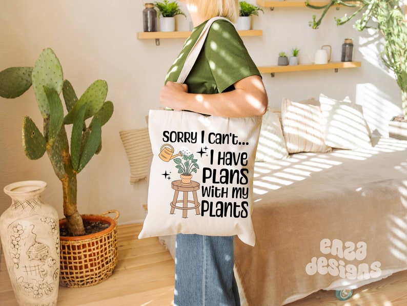 May include: A white tote bag with a black graphic that says "Sorry I can't... I have plans with my plants". The graphic also includes a small potted plant and a watering can.