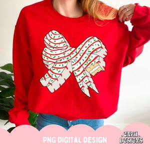 May include: A red sweatshirt featuring a large bow design with white, red, and green accents, resembling a candy cane. The bow has a bite taken out of it. The text "PNG DIGITAL DESIGN" is at the bottom.