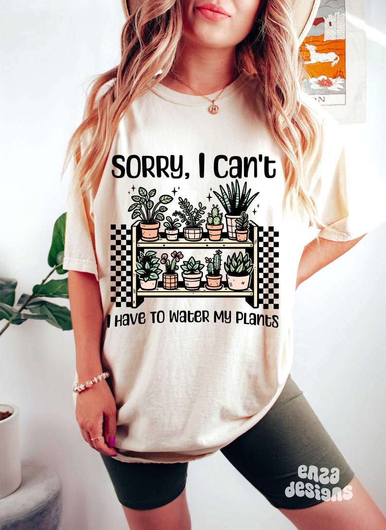 Puede incluir: Una camiseta blanca con el texto "Lo siento, no puedo, tengo que regar mis plantas" y una ilustraci&oacute;n de dibujos animados de un estante con plantas en macetas.