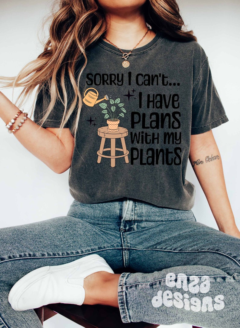 May include: A gray t-shirt with the text "Sorry I can't... I have plans with my plants" and a cartoon illustration of a potted plant on a stool with a watering can pouring water on the plant.