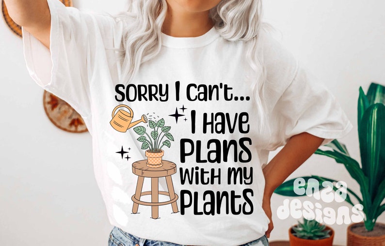 May include: White t-shirt with the text "Sorry I can't... I have plans with my plants."  A cartoon illustration of a potted plant with a watering can pouring water on it is above the text.