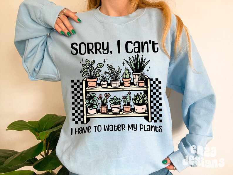Puede incluir: Sudadera azul claro con un gr&aacute;fico de una estanter&iacute;a de plantas con el texto "Lo siento, no puedo, tengo que regar mis plantas".