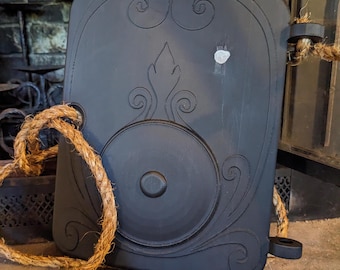 May include: A black wooden door with intricate carvings and a rope handle. The door is closed and has a circular design in the center.