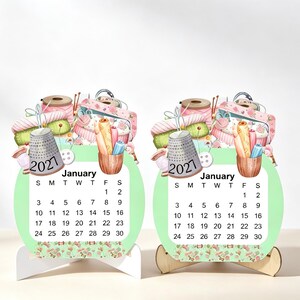May include: Two identical desk calendars for January 2021, each featuring a light green circular background with a watercolour illustration of sewing supplies including a thimble, thread spools, and buttons. The calendar grid is clearly visible.
