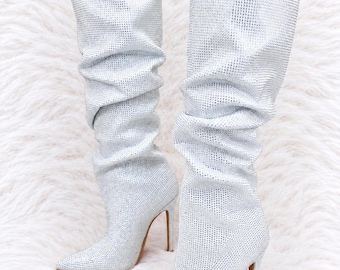 May include: A pair of knee-high boots covered in small, reflective silver rhinestones. These boots feature a pointed toe, a high stiletto heel, and a slouchy, gathered shaft design that creates a textured appearance across the entire surface.