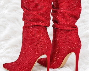 May include: A pair of red mid-calf boots featuring a pointed toe and a high stiletto heel. The entire exterior of the boots is covered in small, reflective red rhinestones, creating a textured, shimmering surface with a slouchy, gathered shaft.