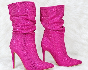 May include: A pair of bright fuchsia mid-calf boots covered in small, reflective rhinestones. These boots feature a slouchy, gathered shaft design, a pointed toe, and a slim, high stiletto heel. The entire exterior surface is textured with crystals.