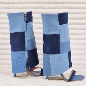 May include: A pair of mid-calf boots featuring a patchwork design of light and dark blue denim fabric. The boots have an open-toe construction, a thin stiletto heel, and a vertical zipper closure on the side of the shaft for a secure fit.