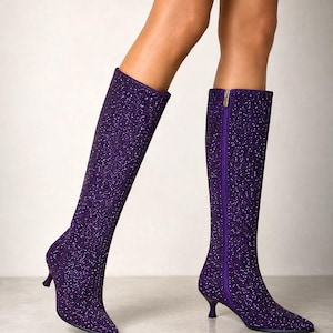 Könnte beinhalten: Ein Paar kniehohe Stiefel in einem tiefen Violett mit durchgehendem Glitzer-Finish. Die Stiefel verfügen über eine spitz zulaufende Zehenpartie, einen schmalen Kitten-Heel-Absatz und einen vertikalen Reißverschluss an der Innenseite.