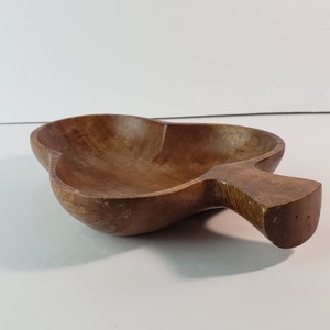 May include: A wooden serving bowl with a handle. The bowl is pear-shaped and made of a dark brown wood. The handle extends from the side of the bowl. The bowl is empty and sits on a white surface.