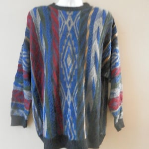 May include: A multi-colored sweater with a geometric pattern. The sweater features a mix of blue, red, gray, and yellow vertical stripes and diamond shapes. It has a crew neck and long sleeves with ribbed cuffs and hem. The sweater is hanging on a white hanger.