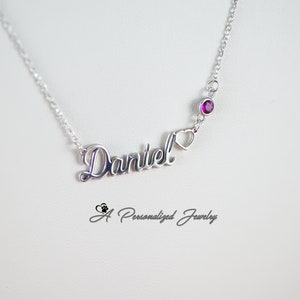 May include: Silver necklace with a cursive name "Daniel" and a small heart charm. A single purple gemstone is attached to the chain above the name.