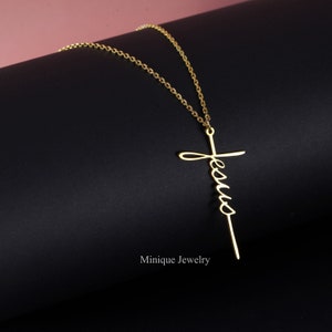 May include: Gold necklace with a delicate chain and a pendant in the shape of a cross with the word "Jesus" written vertically on it.