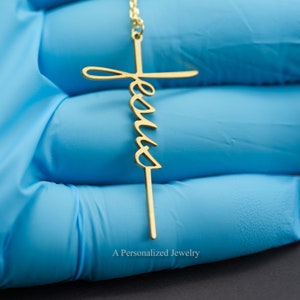 May include: A gold-tone necklace with a delicate cross pendant featuring the word "Jesus" inscribed on it.