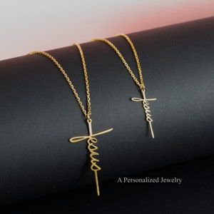 May include: Two gold necklaces with a cursive "Jesus" cross pendant. The necklaces are on a black surface with the text "A Personalized Jewelry" at the bottom.