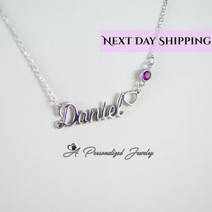 May include: Silver necklace featuring the name "Daniel" in a cursive script, a small heart charm, and a single purple gemstone. The necklace is displayed against a white background with the text "NEXT DAY SHIPPING" and "A Personalized Jewelry" in the bottom corners.