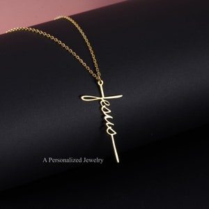 May include: A gold necklace with a cross pendant that has the word "Jesus" written on it in a cursive font.
