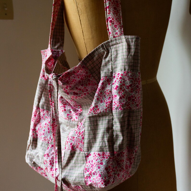 Może przedstawiać: Duża torba typu tote wykonana z patchworku z połączenia r&oacute;żowego materiału w kwiaty i brązowego materiału w kratę. Torba ma sznurek do zamykania i dwa długie paski.