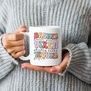 Könnte beinhalten: Weiße Keramiktasse mit einem bunten Design, auf dem "Dasher Dancer Prancer Vixen Whiskey Vodka Tequila Blitzen" steht.