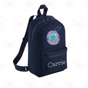 May include: A navy blue backpack with a zipped pocket and a personalised name "Carrie" embroidered on the front. The backpack features a colourful cartoon image of a Tamagotchi.