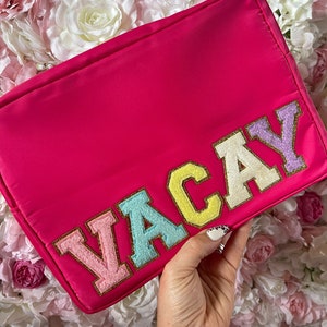 May include: Pink zippered pouch with the word "VACAY" spelled out in colourful felt letters.