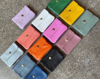 May include: Assortment of 12 small leather wallets in various colors, including pink, blue, green, yellow, and orange. Each wallet has a single gold snap closure.
