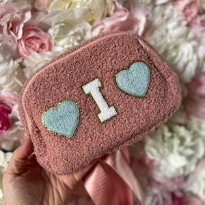 May include: A pink fluffy mini backpack with a white "I" and two blue heart patches.