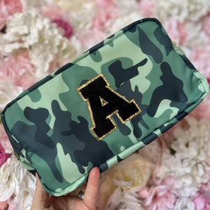 May include: A green and black camouflage makeup bag with a black felt letter "A" with gold glitter trim.