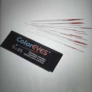 May include: A pack of 25 red-tipped beading needles, size 12, labeled "ColorEyes" with the text "beading needles, aiguilles à perler, agujas para cuentas".