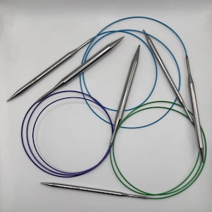 Peut inclure: Cinq paires d'aiguilles à tricoter circulaires de différentes tailles. Les aiguilles sont en métal et ont une finition argentée. Les câbles sont de couleur bleue, verte et violette.