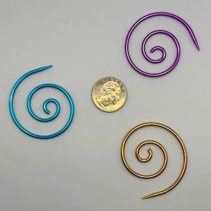 May include: Three metal spiral wire rings in different colors: blue, purple, and gold. The rings are about the size of a US quarter.