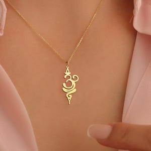 May include: A gold necklace with a delicate pendant featuring the Om symbol. The pendant is intricately designed with a swirling pattern.