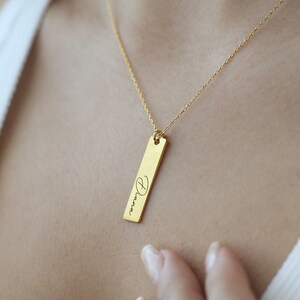 Puede incluir: Un collar de oro con un colgante de barra vertical grabado con el nombre "Diana" en escritura cursiva.