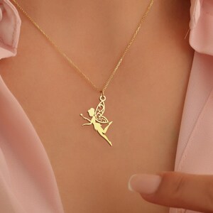 May include: A gold necklace with a delicate fairy pendant. The fairy is depicted with wings and a flowing dress.