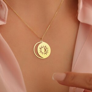 May include: A gold necklace with a pendant featuring a sun and moon design. The pendant is a circle with a crescent moon cut out, and the sun is inside the moon.