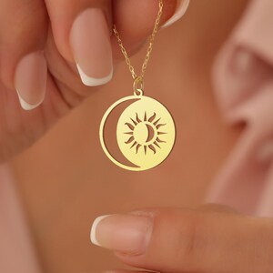 May include: A gold necklace featuring a sun and moon pendant. The pendant is a circular design with a crescent moon on one side and a sun with rays on the other.