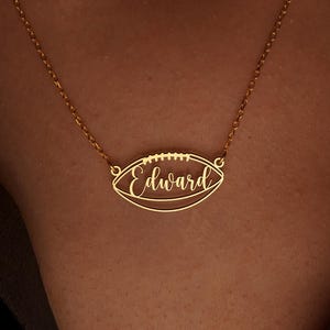 Op de afbeelding: Een goudkleurige ketting met een voetbalvormige hanger. De hanger heeft de naam "Edward" in cursief schrift. De ketting wordt om de nek gedragen.