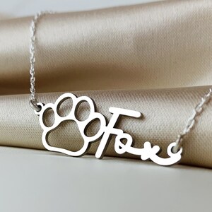May include: Silver necklace with a paw print charm and the name "Fox" written in cursive.