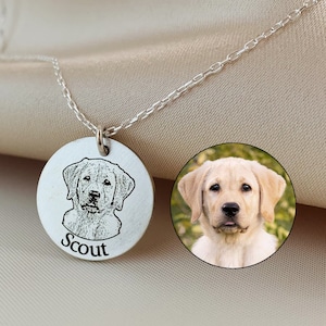 May include: A silver necklace with a circular pendant engraved with a dog portrait and the name "Scout". A small, circular photo of the dog is next to the pendant. The necklace is shown on a beige satin background.
