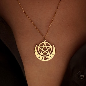 Peut inclure: Collier pendentif dor&eacute; avec un pentagramme dans un croissant de lune. La cha&icirc;ne est fine et le pendentif est port&eacute; sur un fond sombre. Le pendentif comprend trois petites phases lunaires.