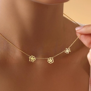 May include: A gold necklace with three delicate flower charms. The necklace is on a model's neck.